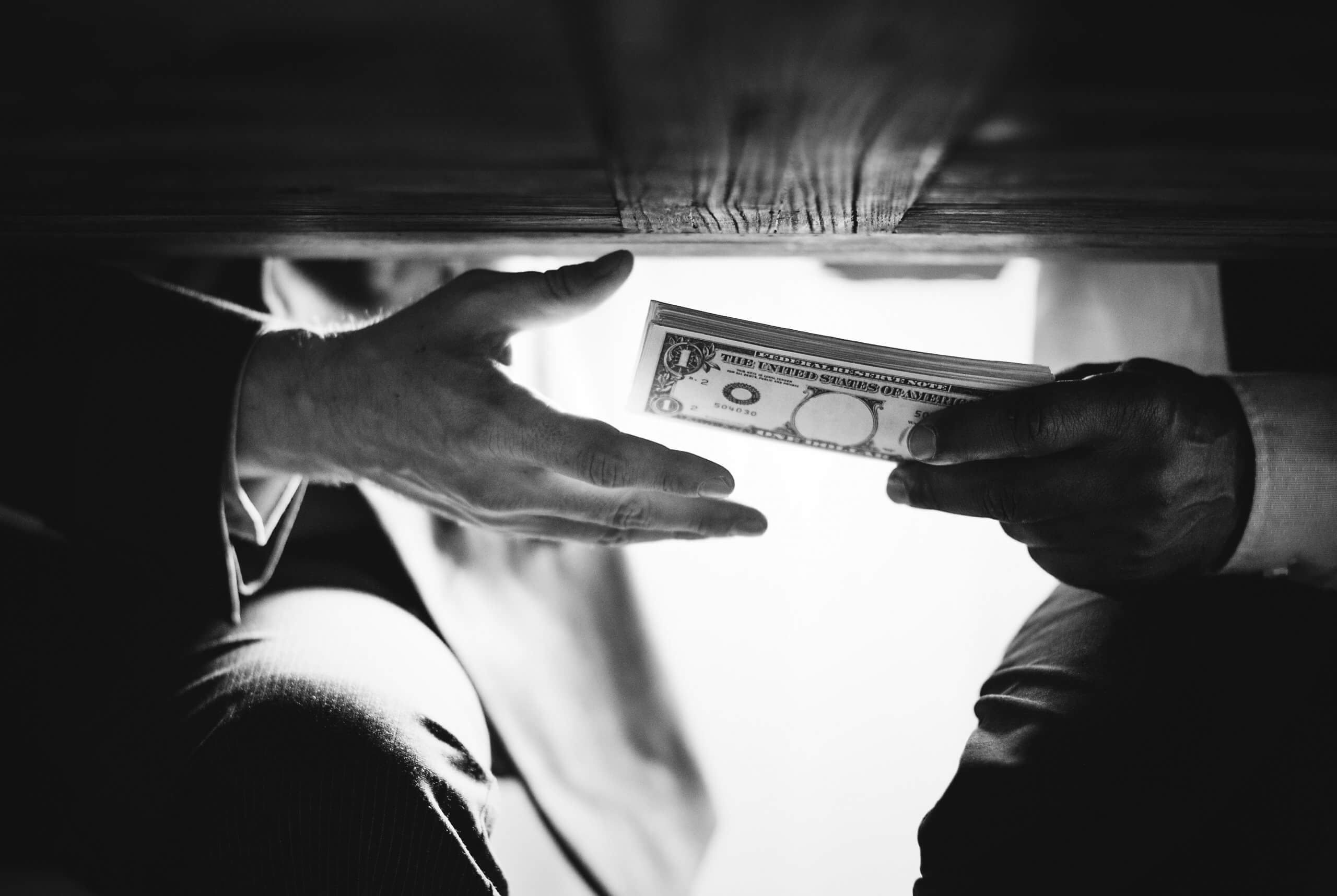 Hands passing money under table corruption bribery ISO 37001 certification audit Malaysia